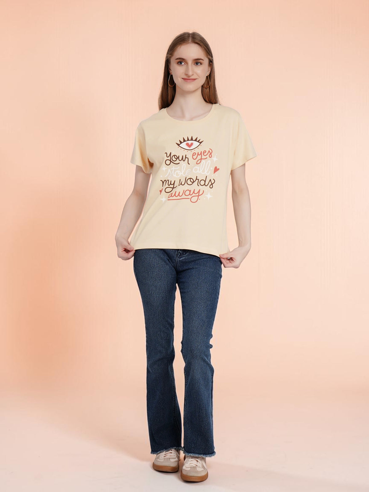 A woman wearing an enaay.com light beige cotton t-shirt with a romantic eye and heart graphic print and dark jeans.