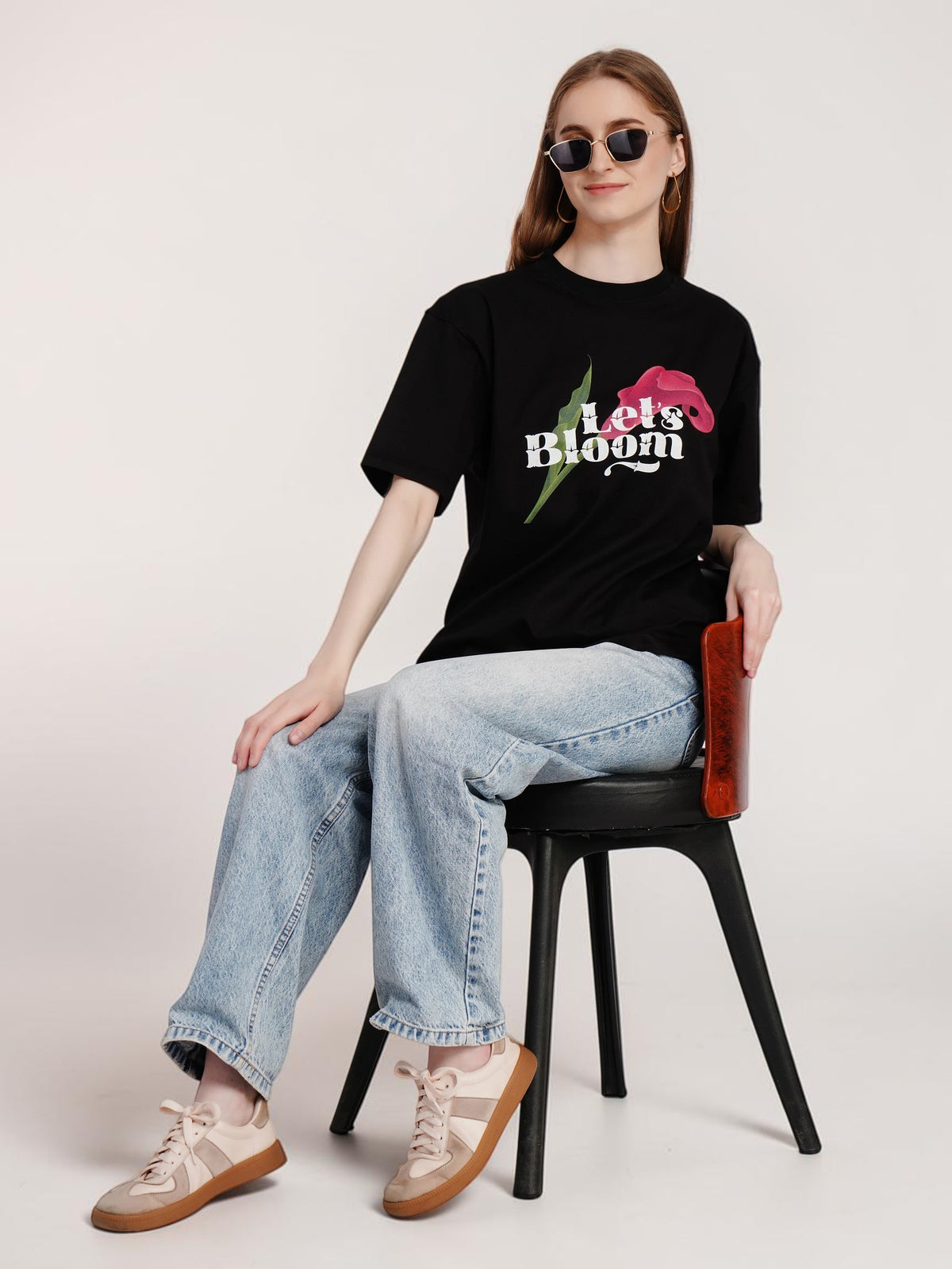 Model wearing an enaay.com black oversized cotton t-shirt with Let's Bloom floral graphic, jeans, and sunglasses.