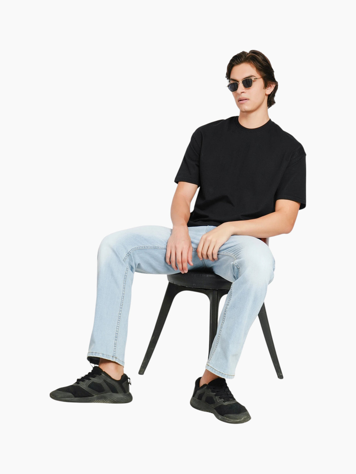 enaay.com men's black oversized crew-neck t-shirt worn by a model sitting on a chair with light wash jeans