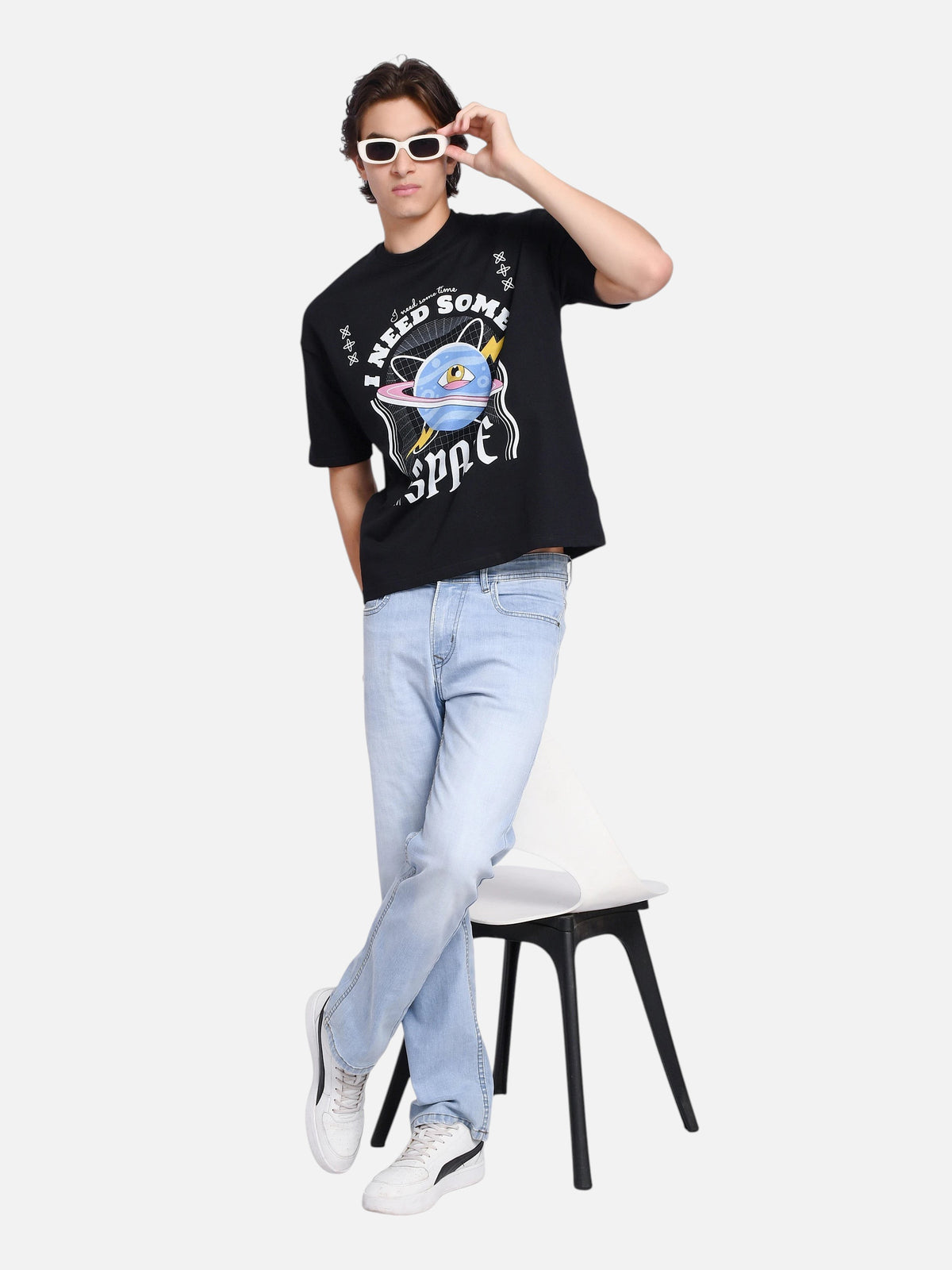 Model wearing enaay.com black oversized graphic t-shirt with cosmic planet print, light wash jeans, and sunglasses.
