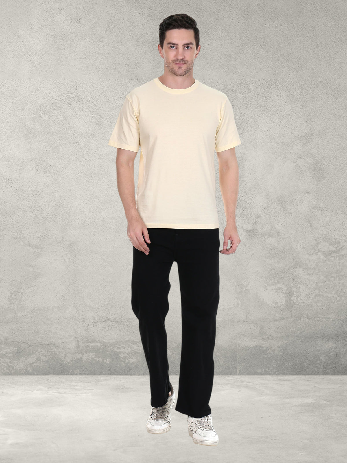 Model wearing an enaay.com cream premium cotton round neck t-shirt with black trousers against a grey wall