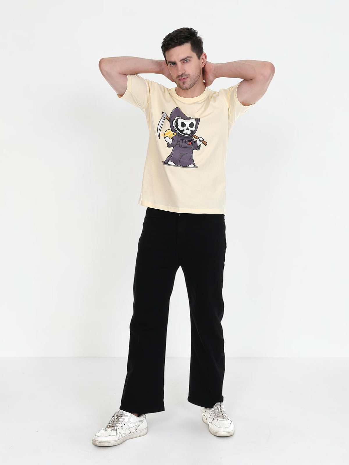 A man wearing an enaay.com cream round neck t-shirt with a cartoon Grim Reaper graphic, paired with black trousers.