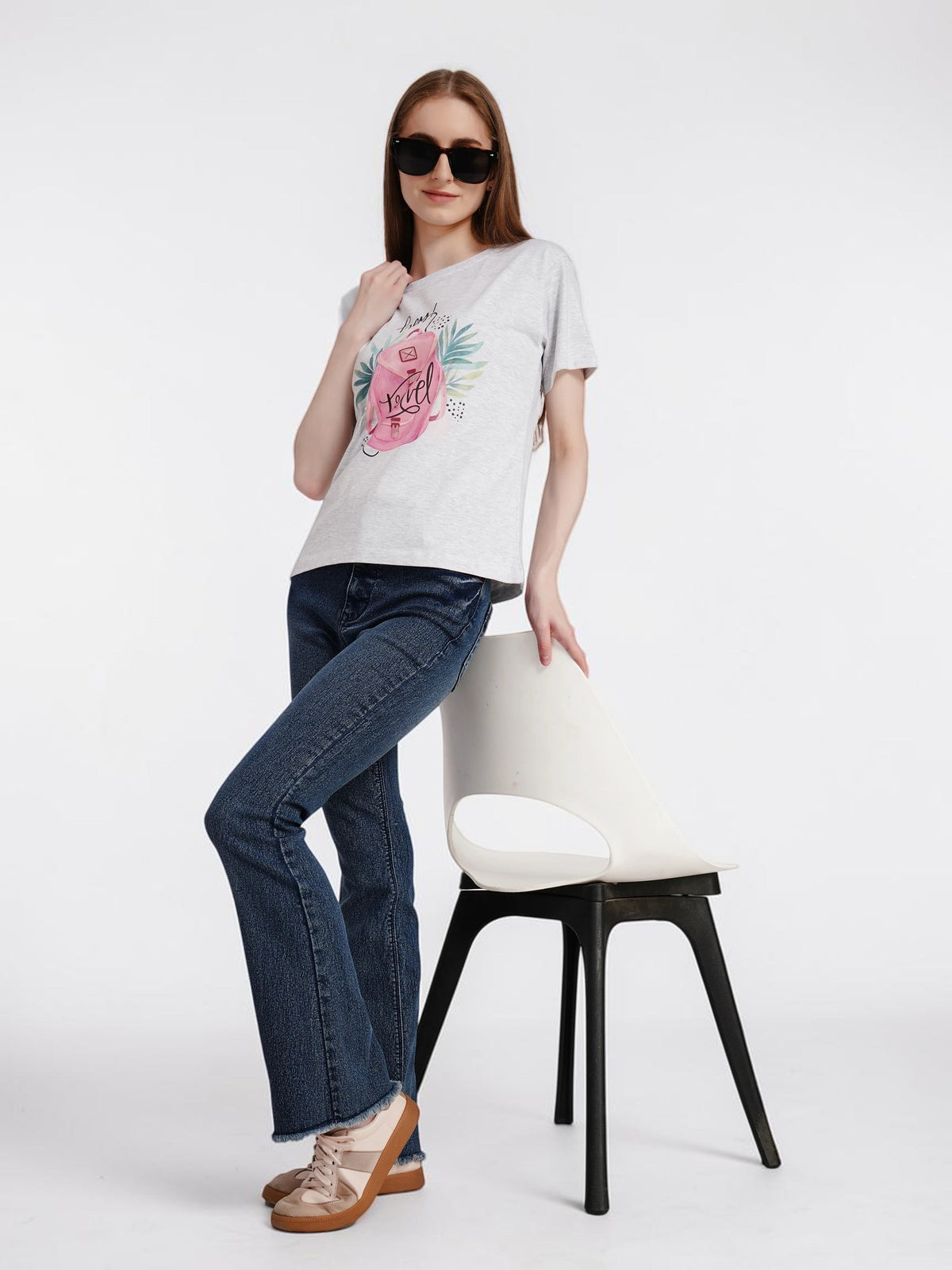 Woman wearing enaay.com light grey melange Hey! Travel graphic cotton t-shirt with jeans and sunglasses by a chair