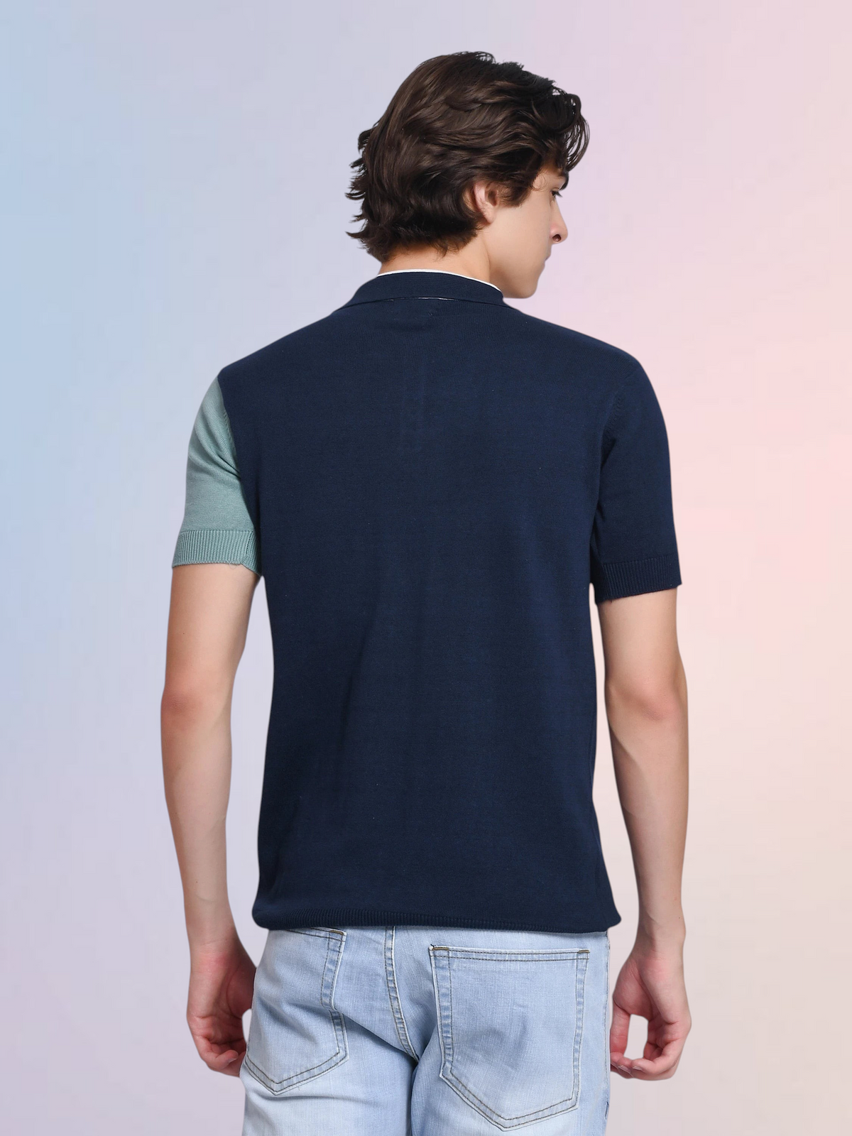 Back view of a man wearing an enaay.com navy blue, white, and sage green colorblock cotton knit polo shirt with jeans.