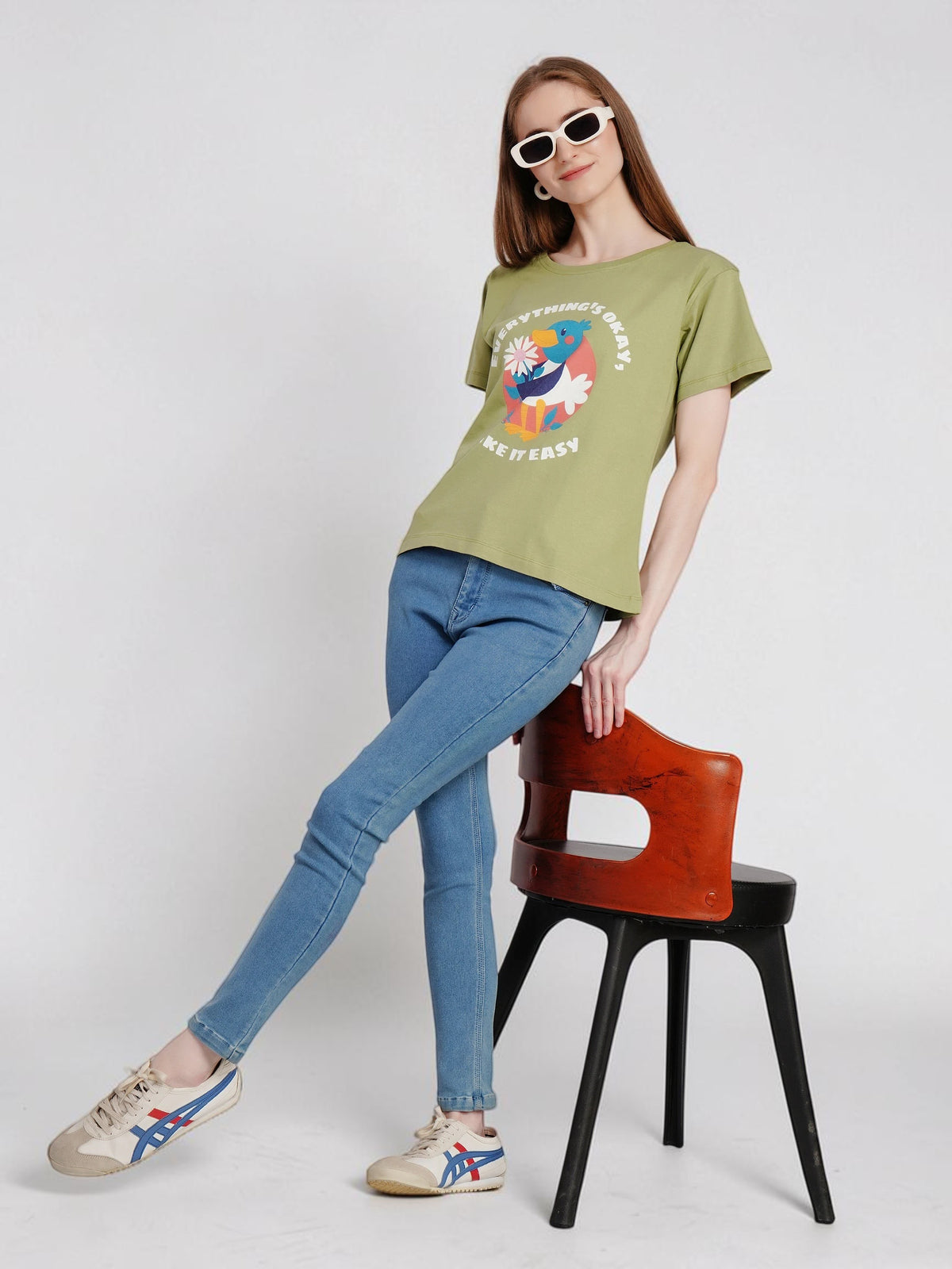 Model wearing enaay.com olive green cotton graphic t-shirt with toucan print, blue jeans, and white sneakers.