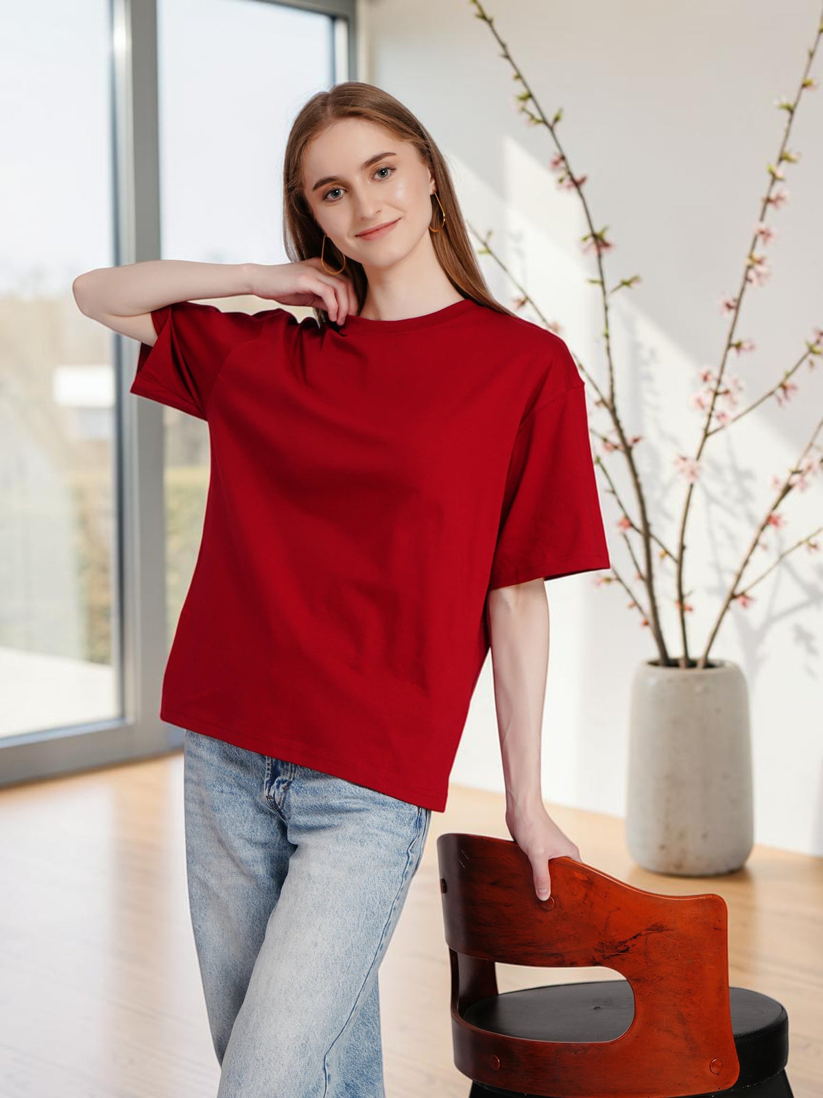 Model wearing an enaay.com red oversized premium cotton t-shirt with blue jeans in a bright indoor setting