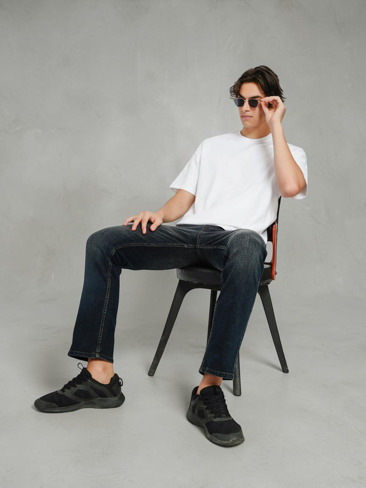 Model wearing an enaay.com white oversized crew-neck t-shirt with dark jeans and black sneakers while seated