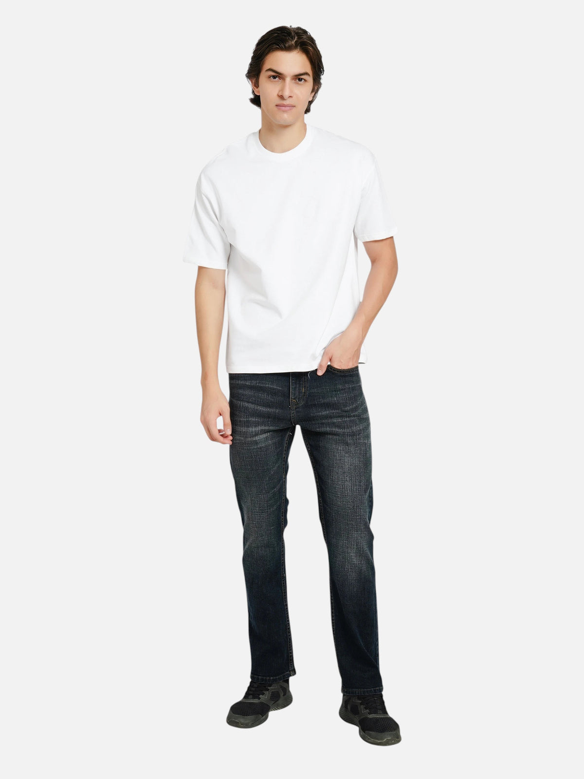 A man wearing an enaay.com white oversized crew-neck t-shirt with dark denim jeans and black sneakers.