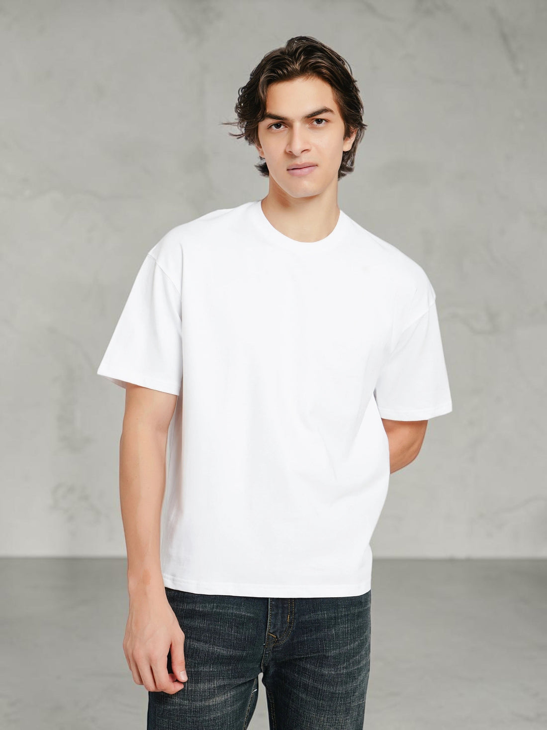 Model wearing an enaay.com white oversized crew-neck t-shirt with dropped shoulders and a boxy fit against a grey wall