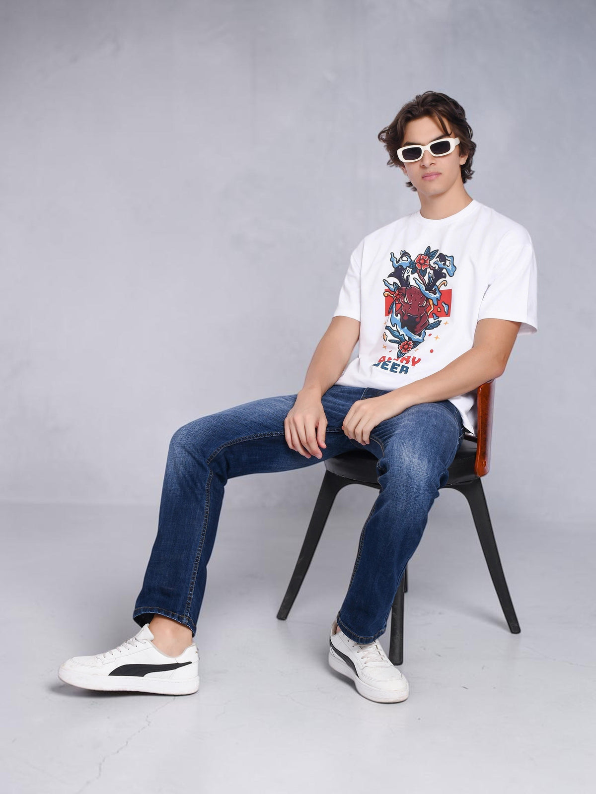 Model wearing enaay.com white oversized t-shirt with angry deer graphic, blue jeans, and white sunglasses
